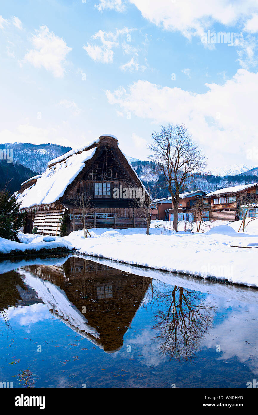 Legno casa di villaggio con Snow capped tetto con mountain range sull orizzonte riflettendo nel lago in inverno, villaggio di Shirakawa Foto Stock Legno casa di villaggio con Snow capped tetto con mountain range sull orizzonte riflettendo nel lago in inverno, villaggio di Shirakawa Foto Stock