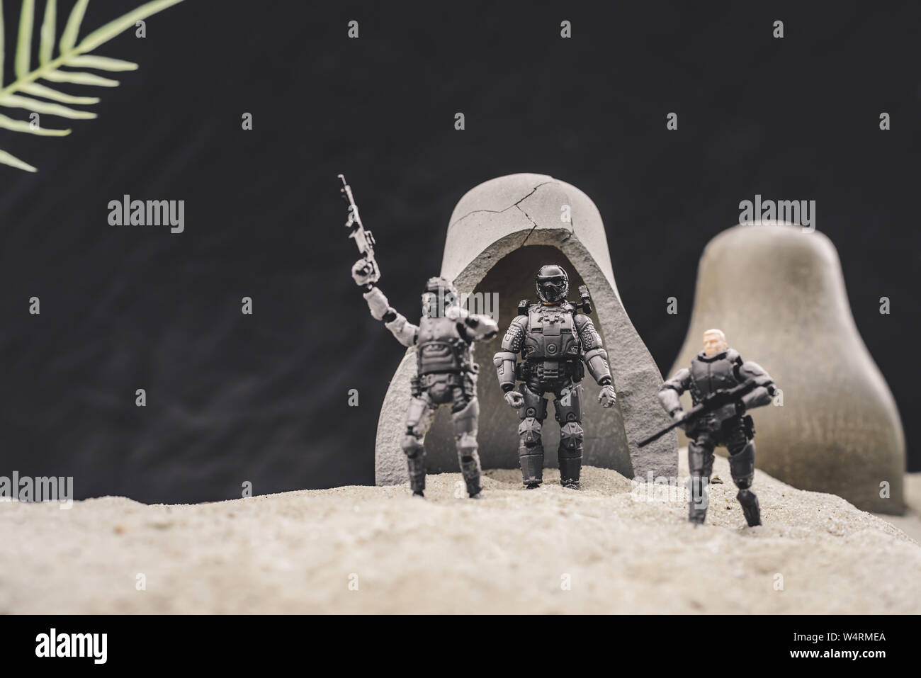Toy Soldiers con pistole e bandiera americana in piedi vicino grotte sulla duna di sabbia su sfondo nero Foto Stock