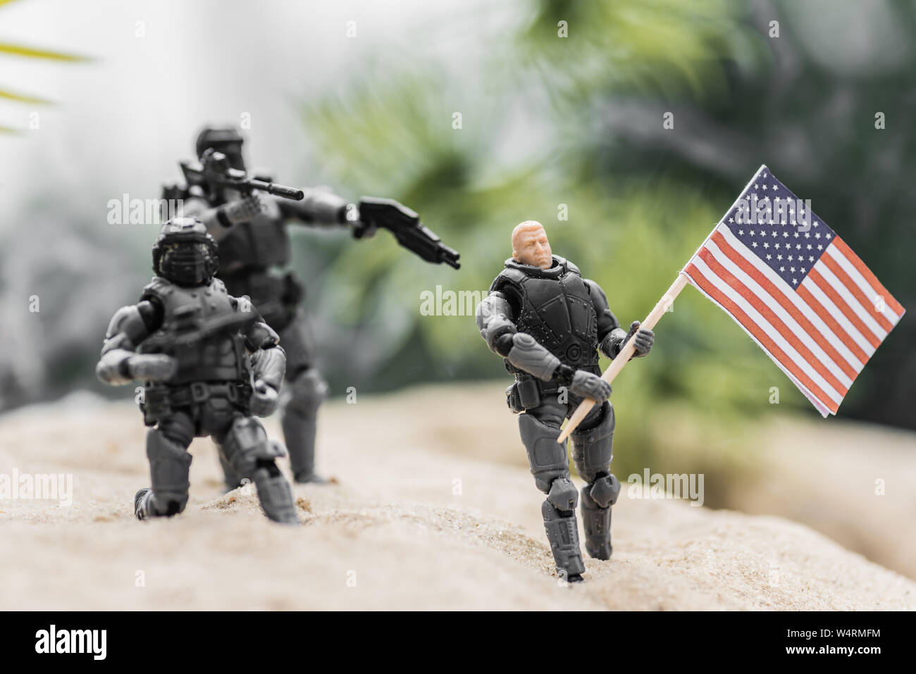 Messa a fuoco selettiva di soldatini mirando con pistole giocattolo all uomo con la bandiera americana sulla collina di sabbia Foto Stock