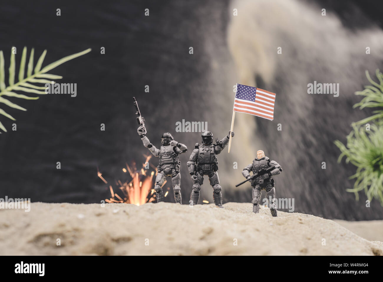 Messa a fuoco selettiva di soldatini con pistole e bandiera americana in piedi vicino all'esplosione sulla duna di sabbia Foto Stock