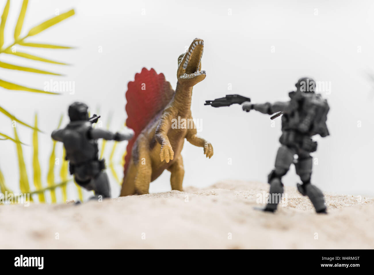Messa a fuoco selettiva di toy soldiers pistole di puntamento su ruggente minuscolo dinosauro su sand hill Foto Stock