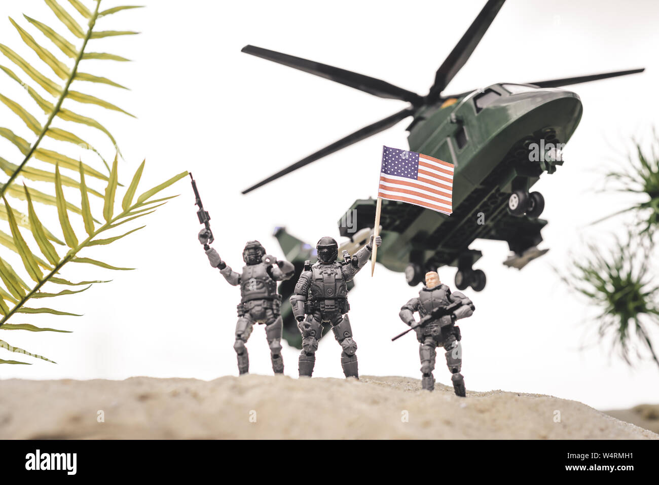 Giocattolo di plastica soldati sulle dune di sabbia con le pistole e bandiera americana vicino copter nel cielo Foto Stock
