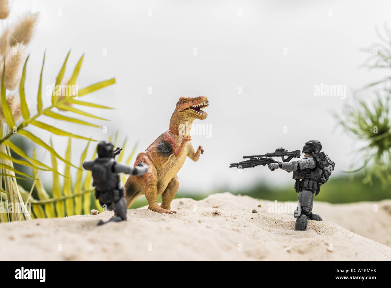 Toy Soldiers mirando con pistole giocattolo a dinosauro su sand hill Foto Stock