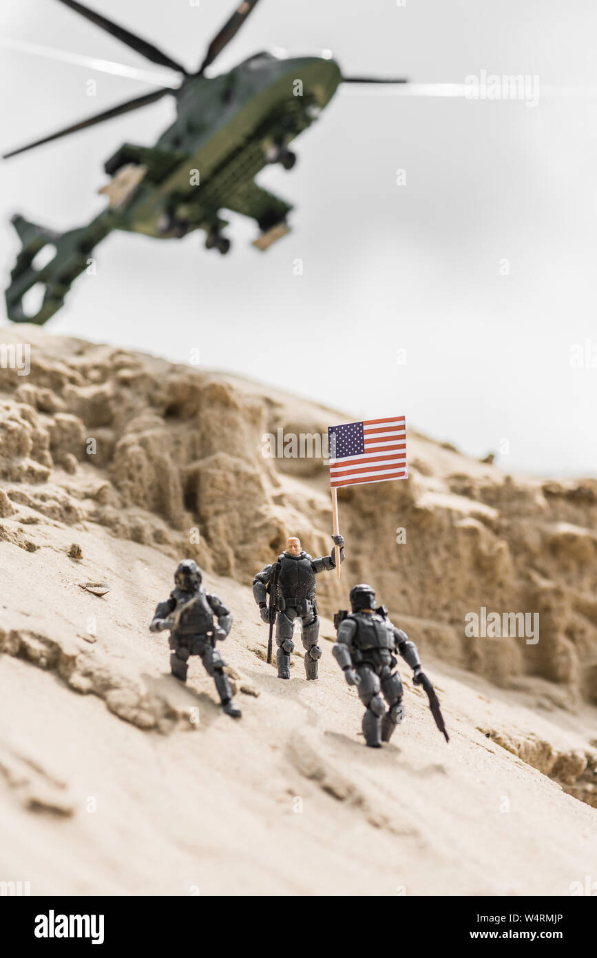 Messa a fuoco selettiva di soldatini sulla collina di sabbia con bandiera americana e elicottero sullo sfondo Foto Stock