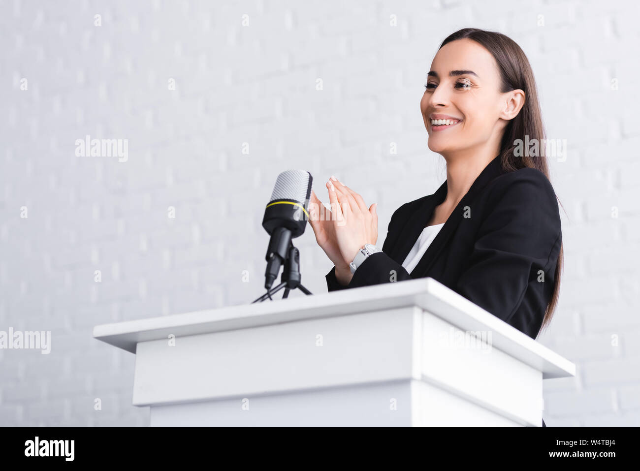 Altoparlante felice battendo le mani mentre si sta in piedi sul podio tribune nella sala conferenze Foto Stock