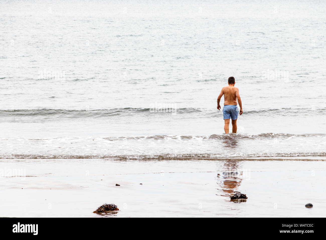 Un singolo nuotatore maschio si innamora nel mare per rinfrescarsi in mare a Buck's Mills con l'aumento delle temperature, Devon, Regno Unito Foto Stock