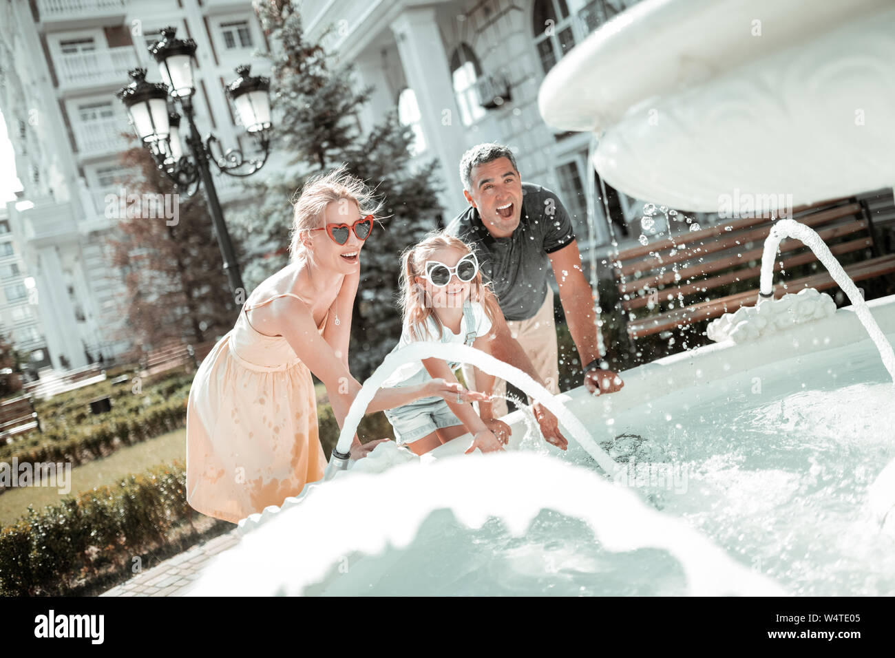 Divertimento estivo. Madre, padre e figlia di ridere e di lavarsi le mani in una fontana al di fuori. Foto Stock