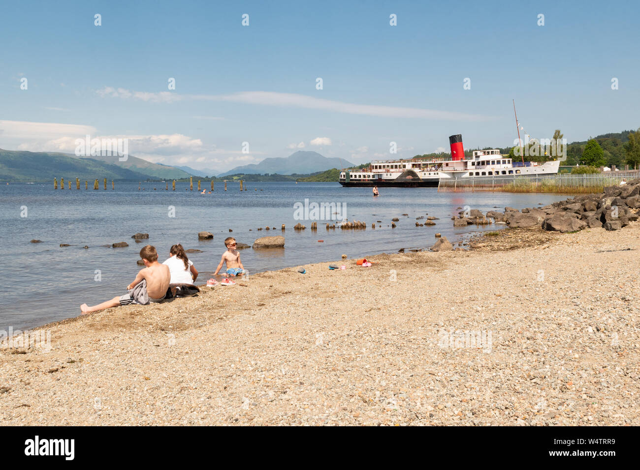Loch Lomond Shores, Balloch, Scotland, Regno Unito - 25 Luglio 2019: Regno Unito - previsioni del tempo - Come temperature aumento a 28 gradi Giovanni, Giuseppe e grazia raffreddare in fondali bassi di Loch Lomond, contro il magnifico sfondo di Ben Lomond e la cameriera del Loch battelli a vapore: Credito Kay Roxby/Alamy Live News Foto Stock