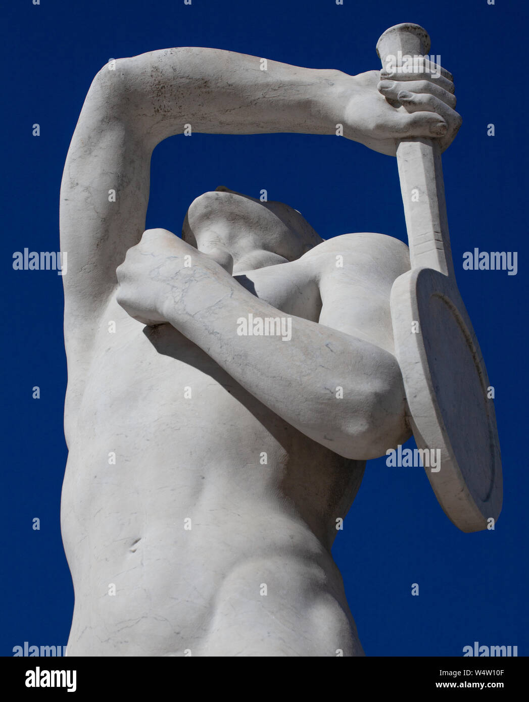 Una statua di pietra di un giocatore di tennis in Stadio dei Marmi (Marmo Stadium) in Roma. La statua ha il suo braccio sollevato per servire contro un Cielo di estate blu. Foto Stock