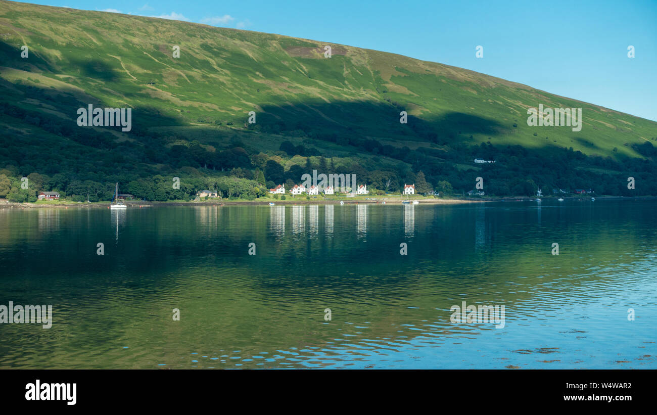 La splendida costa intorno al Kyles of Bute, immagine di Colintraive case con riflessioni presi da Rhubodach, Isle of Bute Foto Stock