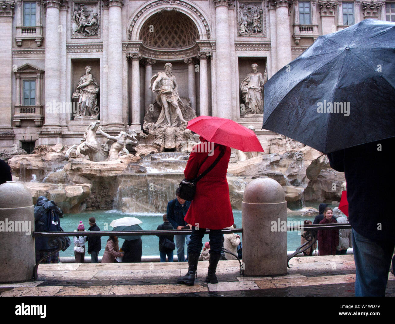 Un giorno di pioggia in Roma, Italia. Donna vestita di un cappotto rosso tenendo un ombrello rosso si fermò di fronte alla fontana di Trevi. Foto Stock