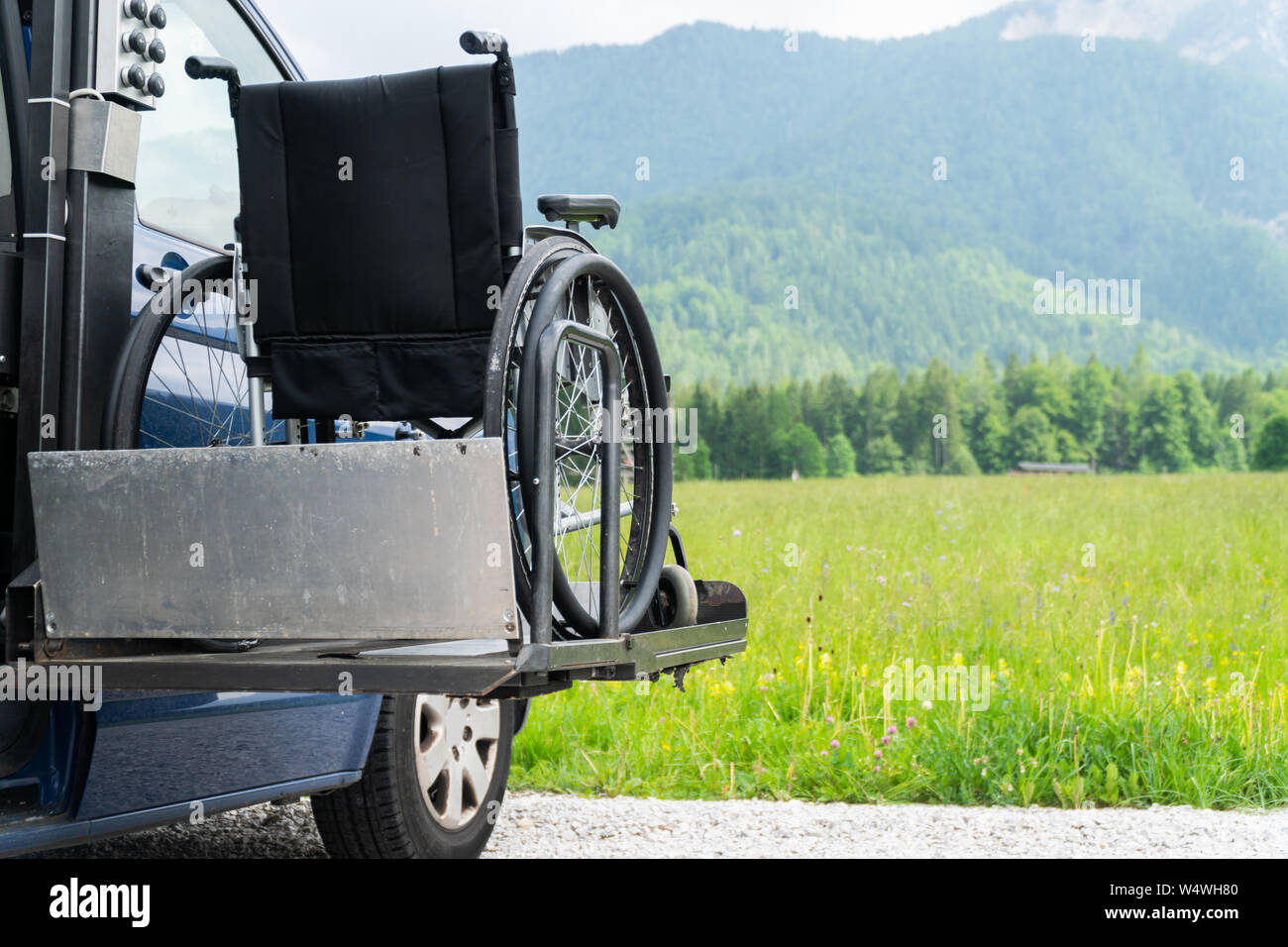 Il nero di sollevamento elettrico veicolo specializzato per le persone con disabilità. Sedia a rotelle vuota su una rampa con la natura e le montagne nella parte posteriore Foto Stock