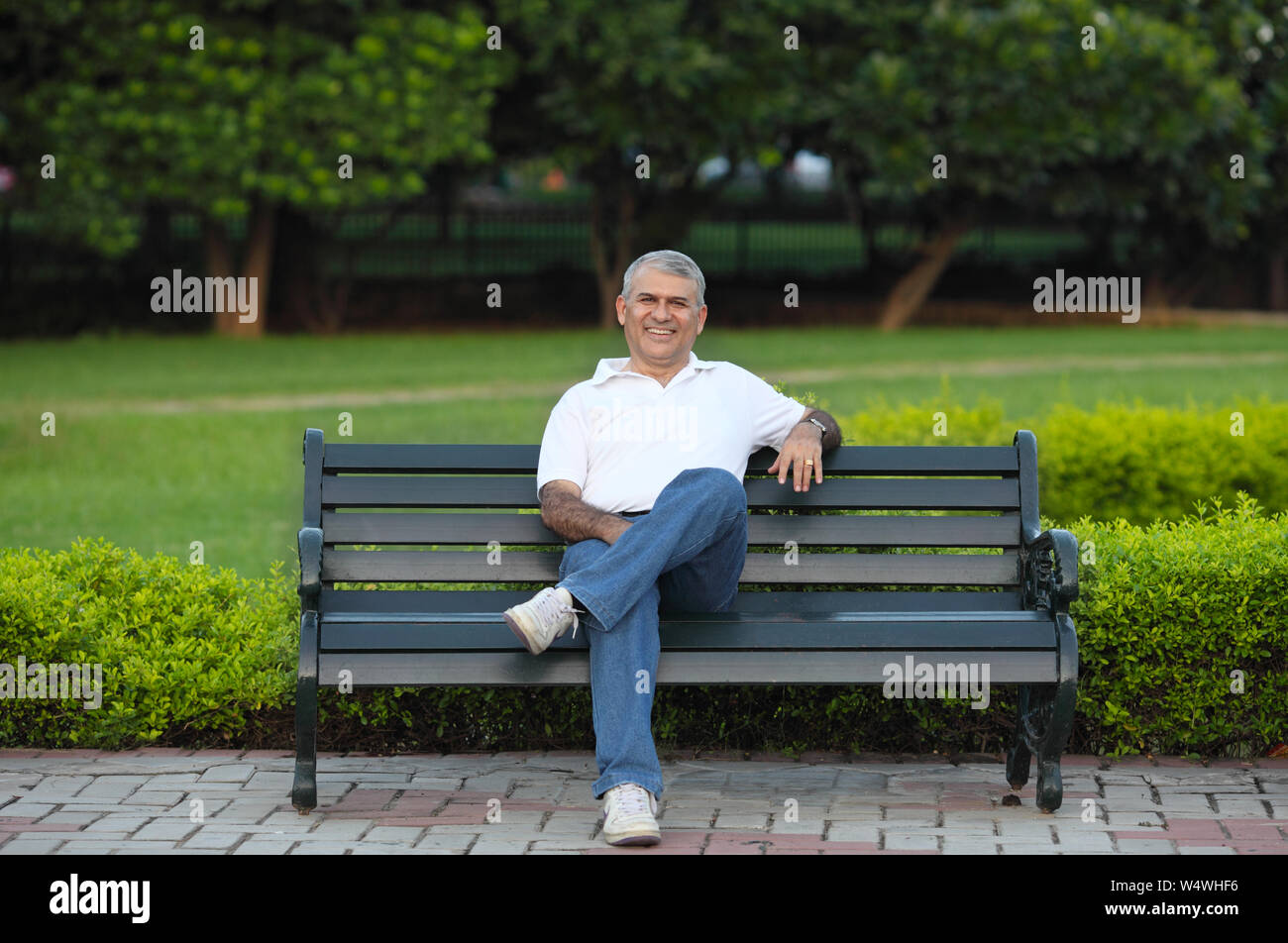 Uomo seduto su una panchina nel parco e sorridente Foto Stock