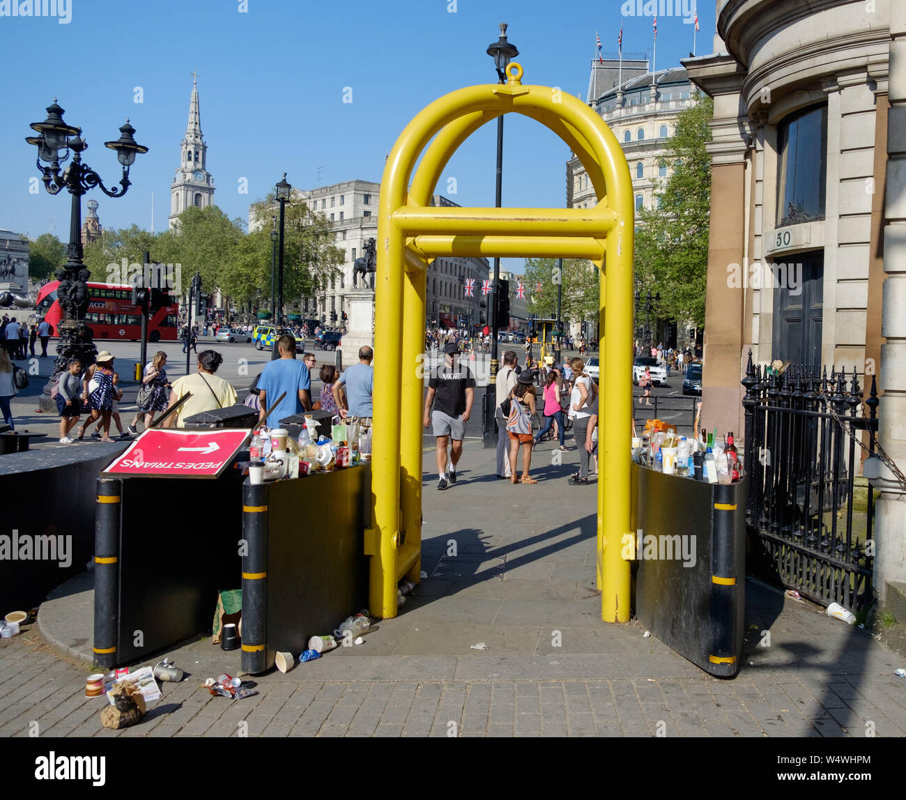 Giallo anti-terrorismo barriere vicino a Trafalgar Square nel centro di Londra, Inghilterra. Con bicchieri vuoti, bottiglie e cestino su ogni lato e la massa. Foto Stock