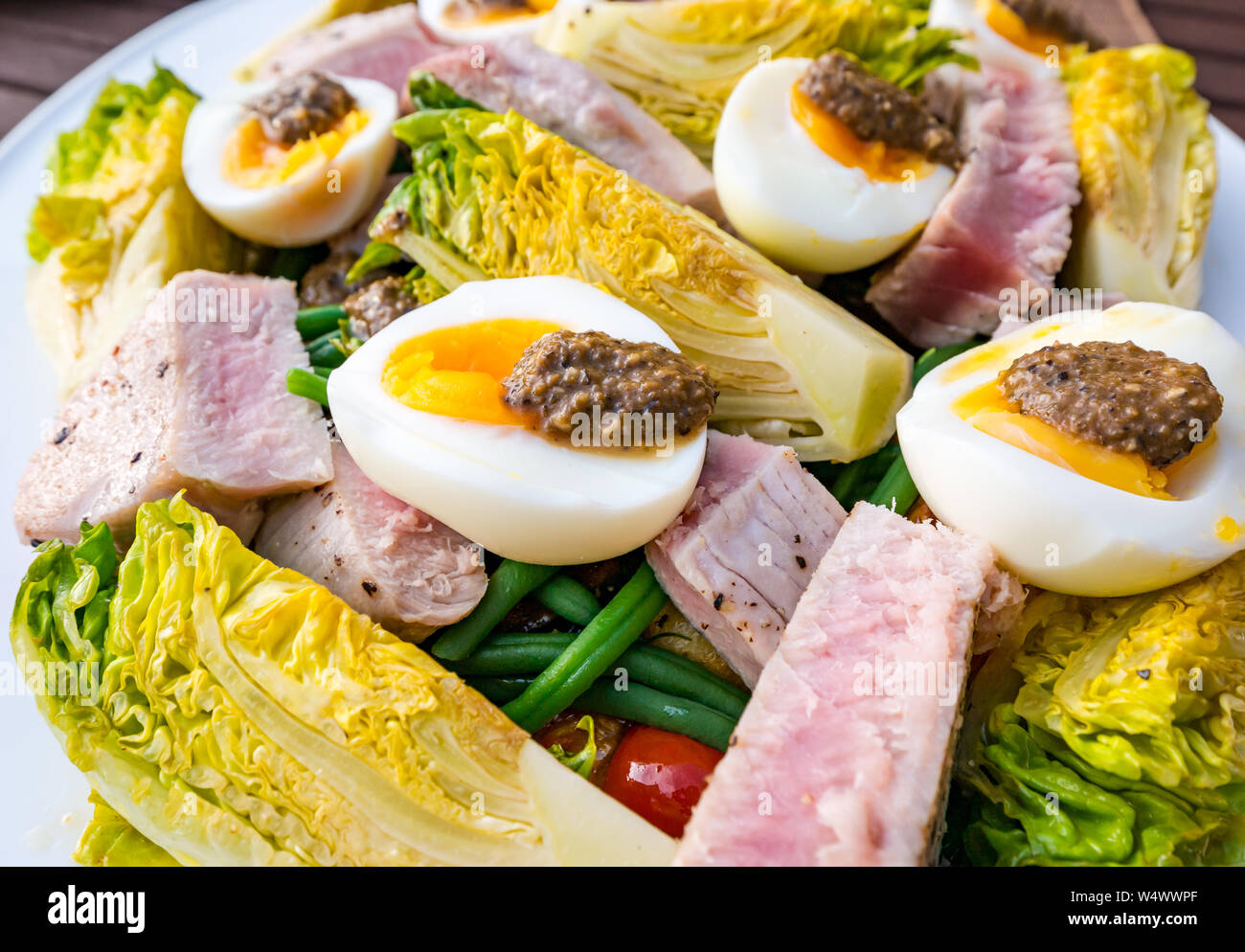 Versione di Insalata Nizzarda sulla piastra bianca. Uova sode e condimento di olive, baby gem lattuga, patate bollite e bistecca di tonno fette Foto Stock