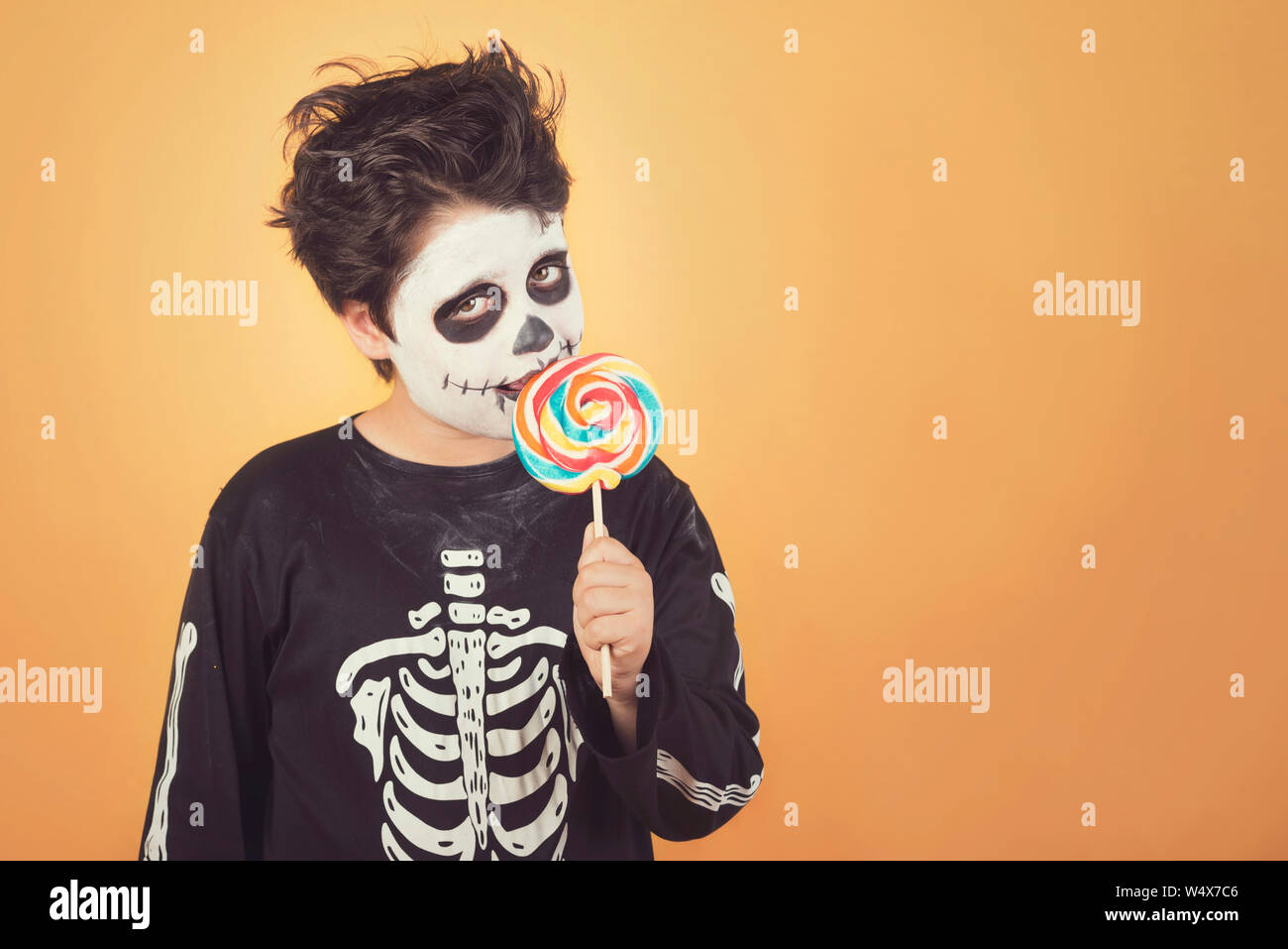 Happy Halloween.divertente bambino in un costume di scheletro di mangiare lecca-lecca di halloween su sfondo arancione Foto Stock