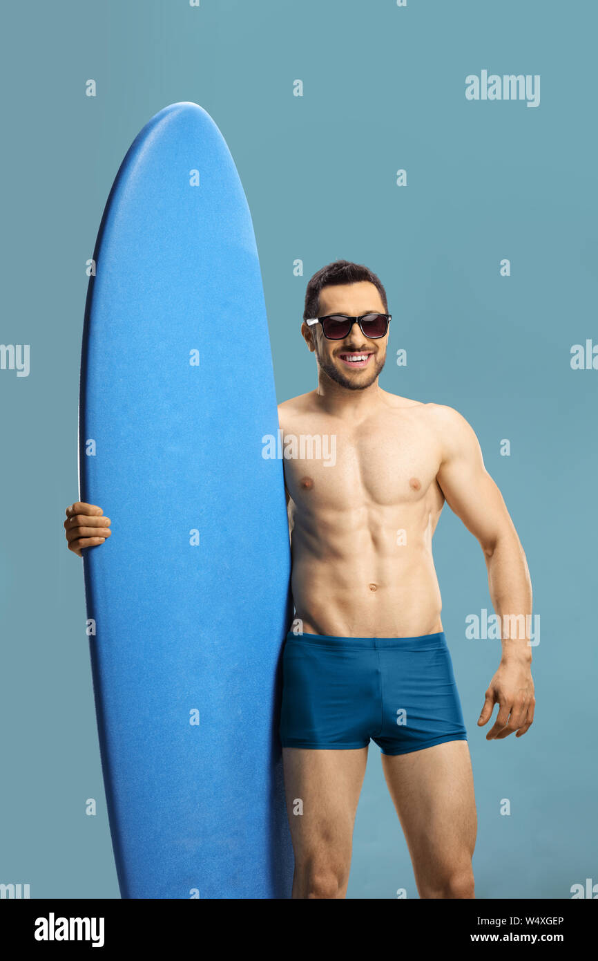 Giovane ragazzo muscolare tenendo un surf board isolato su sfondo blu Foto Stock