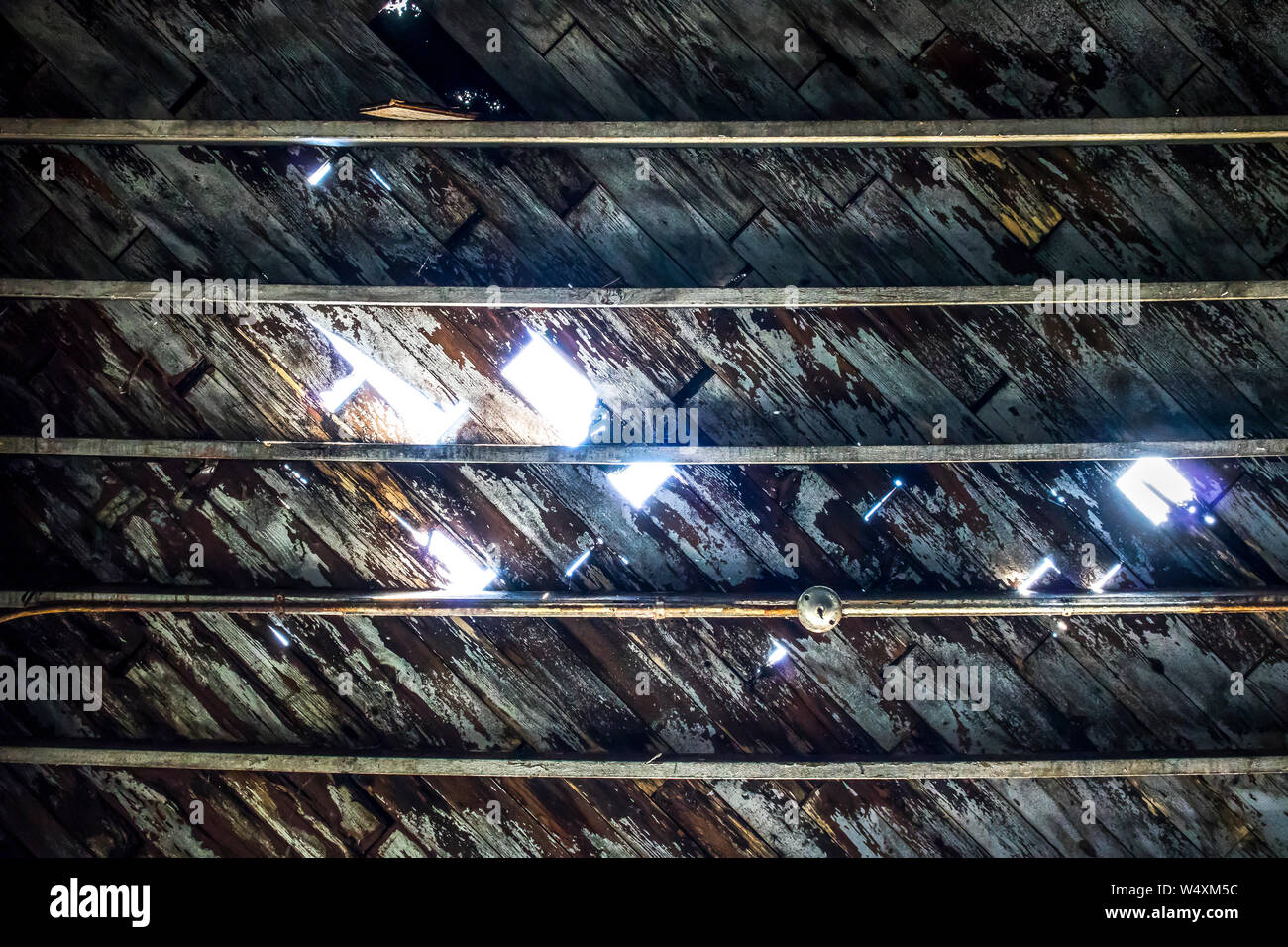 Peeling su vernice vecchia soffitto in legno presa dal basso. Luce entra attraverso dove le assicelle hanno eroso in industriali abbandonati cannery magazzino. Foto Stock