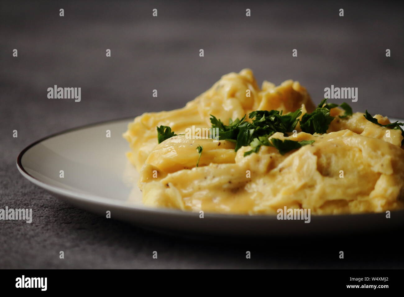 Uova strapazzate su piastra bianca con prezzemolo e burro. Dark e moody cibo fotografia. Una sana prima colazione, il pranzo e la cena. Foto Stock