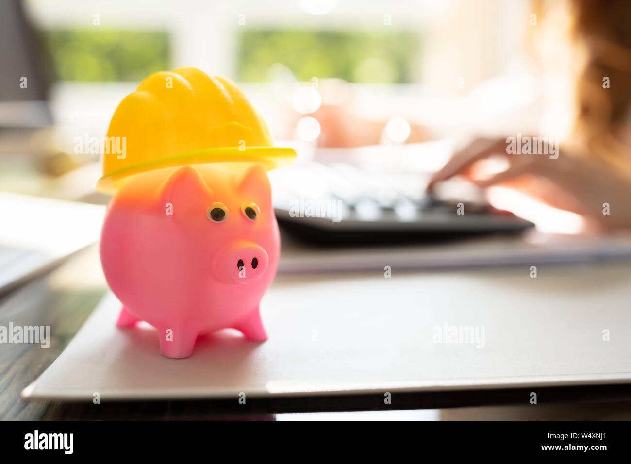 Close-up di Rosa Piggybank con Casco giallo sulla scrivania in ufficio Foto Stock