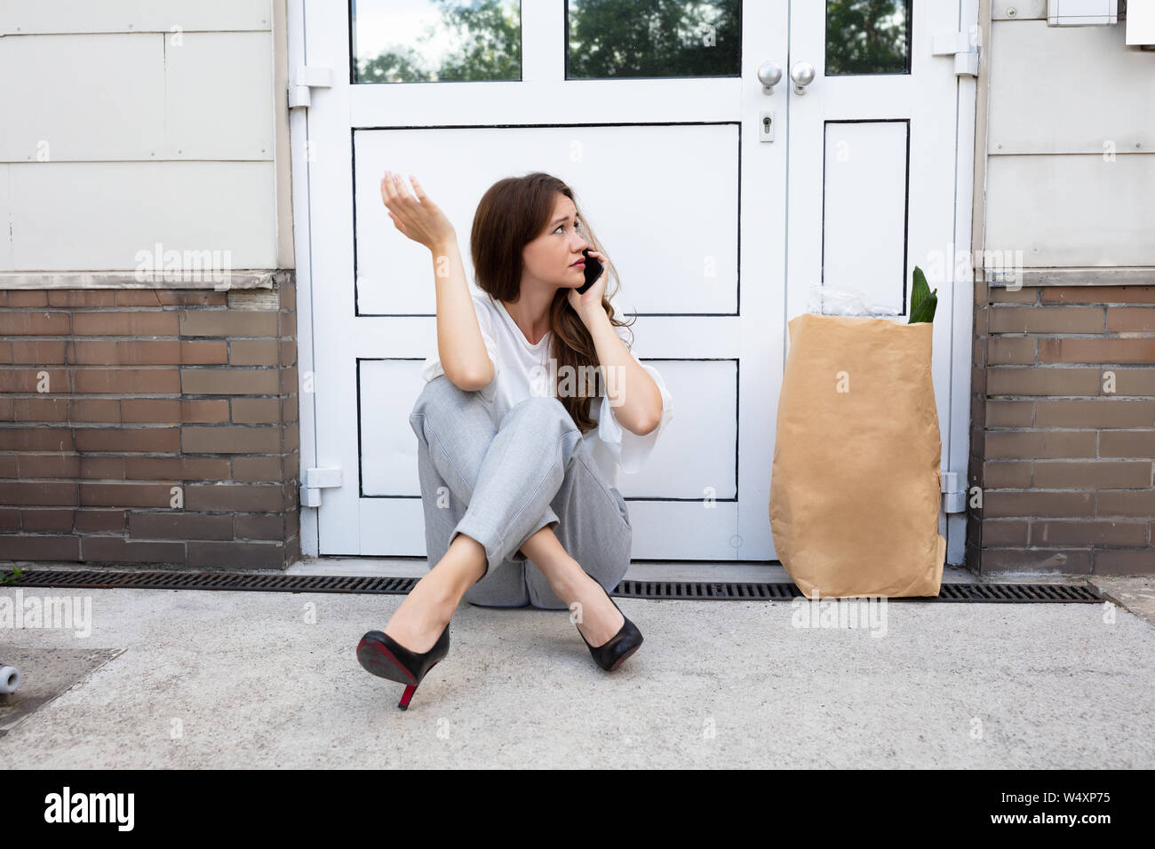 Una paura giovane donna seduta al di fuori della porta a parlare su Mobilephone Foto Stock