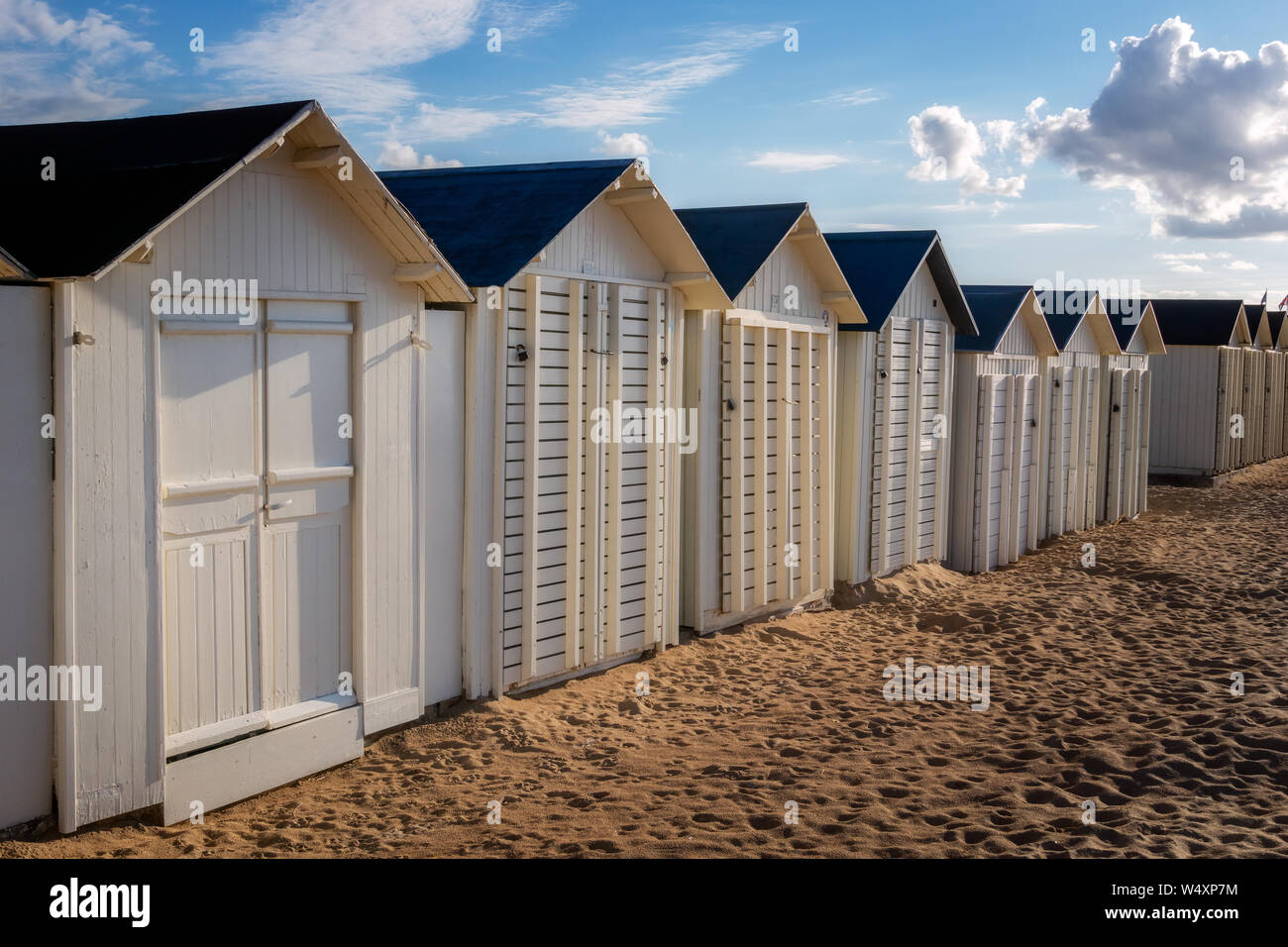 Riga bianca di cabine in legno o cabine a fianco di Riva Bella sulla spiaggia la sera presto, Ouistreham, Normandia, Francia. Foto Stock