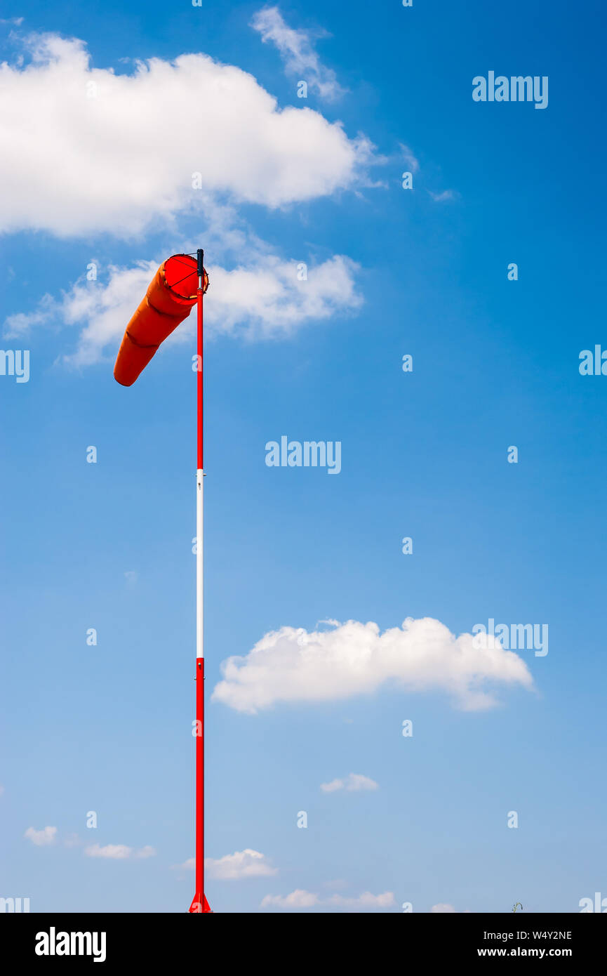 Indicatore del vento in pole nella brezza contro il cielo blu e nuvole cumulus. Foto Stock