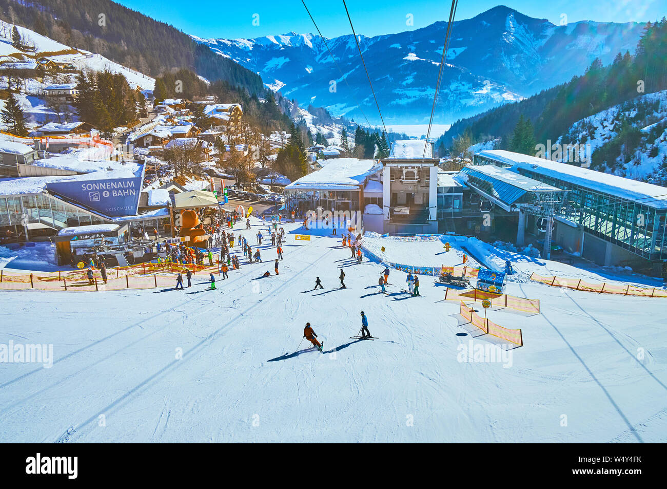 ZELL AM SEE, Austria - 28 febbraio 2019: emozionante viaggio sulla moderna funivia con una vista sulla sua stazione inferiore, sciatori sul monte Shcmitten piste Zel Foto Stock