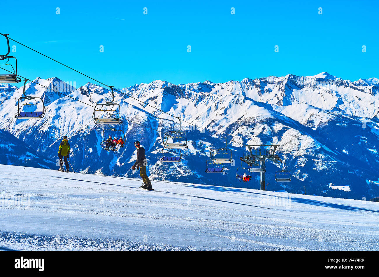 ZELL AM SEE, Austria - 28 febbraio 2019: lo snowboarder e sciatori godetevi il viaggio lungo il pendio del monte Schmittenhohe con una vista sul Kapell Foto Stock