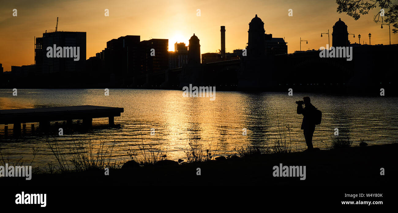 Il tiro è Boston, sulla sponda del fiume Charles nel crepuscolo. Immagine di un fotografo di scattare le foto. Il cielo giallo riflette sul fiume. Foto Stock