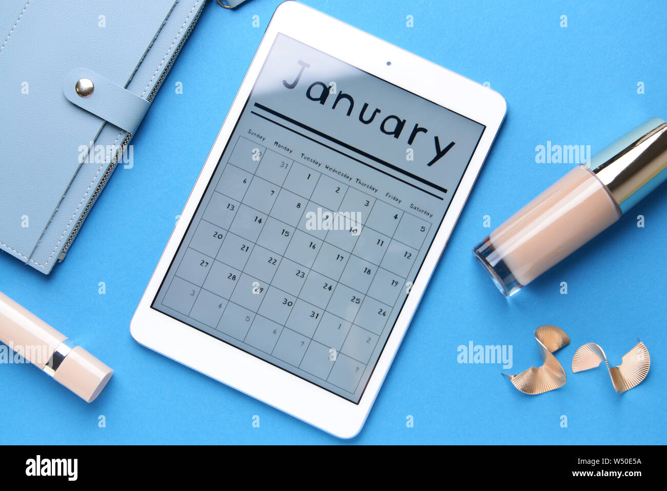 Tablet PC con il calendario sullo schermo, cosmetici e portafoglio sul colore di sfondo Foto Stock