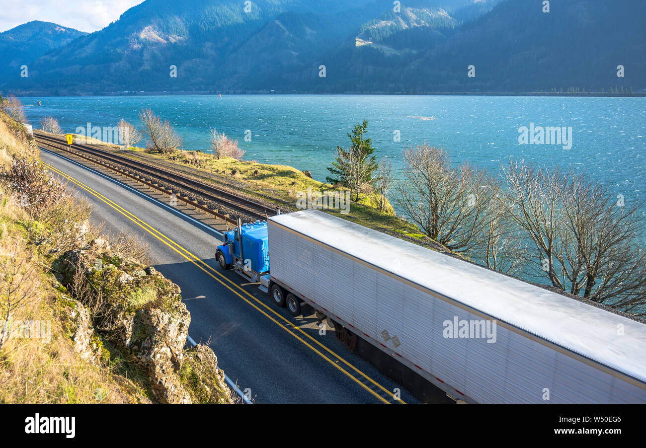 Big Rig classic American potente semi blu carrello refrigerato con semi rimorchio il trasporto di merci surgelate in esecuzione su strada lungo la ferrovia e di rive Foto Stock