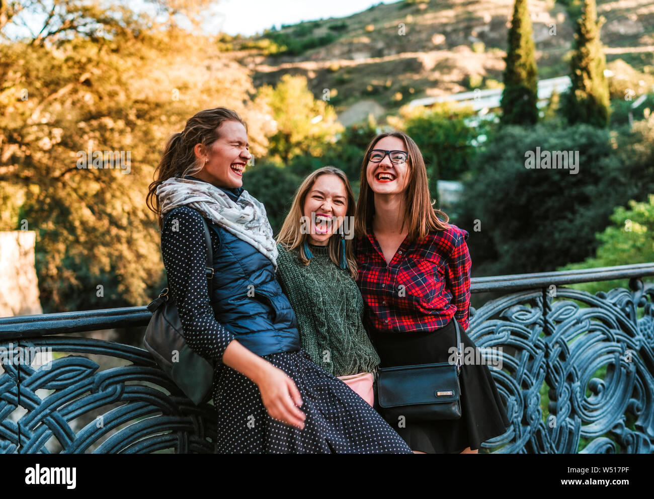 Tre giovani donne in piedi sul ponte in parco a fine giornata estiva di ridere Foto Stock