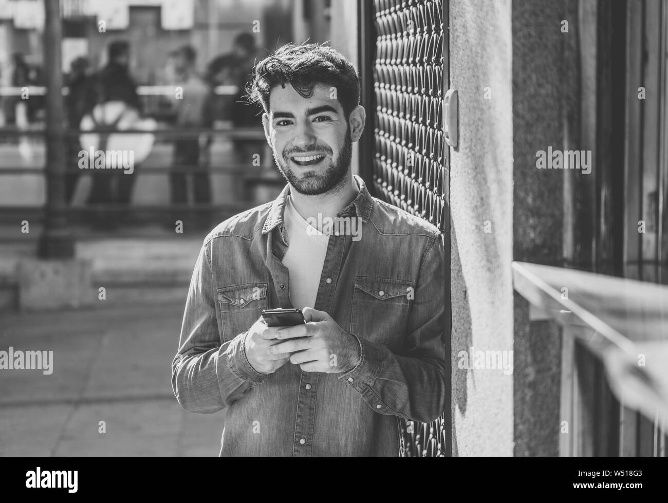 Moda uomo college nel suo ventenne felice controllo blog o chattare su internet con amici su smart telefono mobile app in unione all'aperto della città. Foto Stock