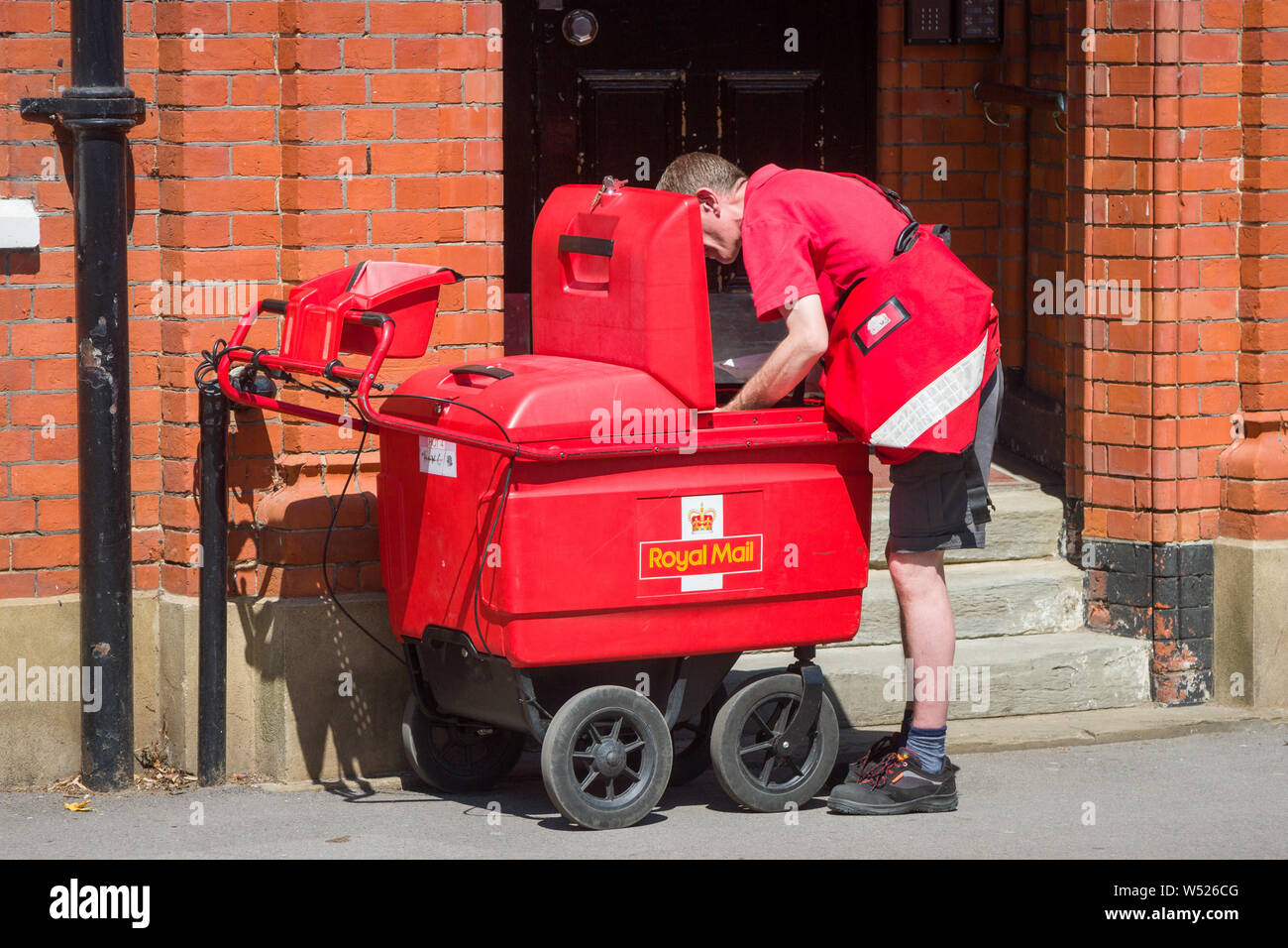 Un postino raccoglie posta per la spedizione da un elettrico round postale Royal Mail delivery carrello o carrello a mano Foto Stock