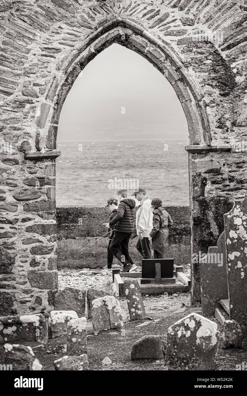 Gruppo di famiglia passando per arcata in pietra di Abbazia in rovina in Ballinskelligs, nella contea di Kerry, Irlanda Foto Stock