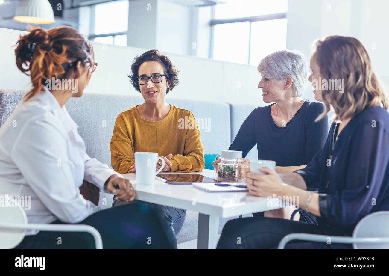 Un gruppo di donne d'affari sedute a tavola che parlano davanti a un caffè. team aziendale durante una pausa caffè in ufficio. Foto Stock