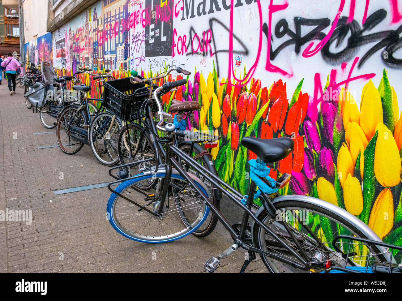 Biciclette olandesi nella parte anteriore di un grande poster del Dutch Canal alloggiamento e tulipani e con graffiti. Foto Stock