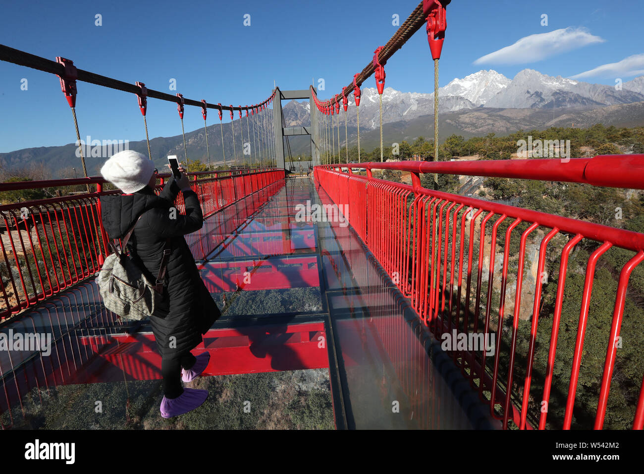 Visitatori posano per foto su con il fondo di vetro suspension bridge spanning su un canyon al Jade Dragon Snow Mountain scenic area a Lijiang, così Foto Stock