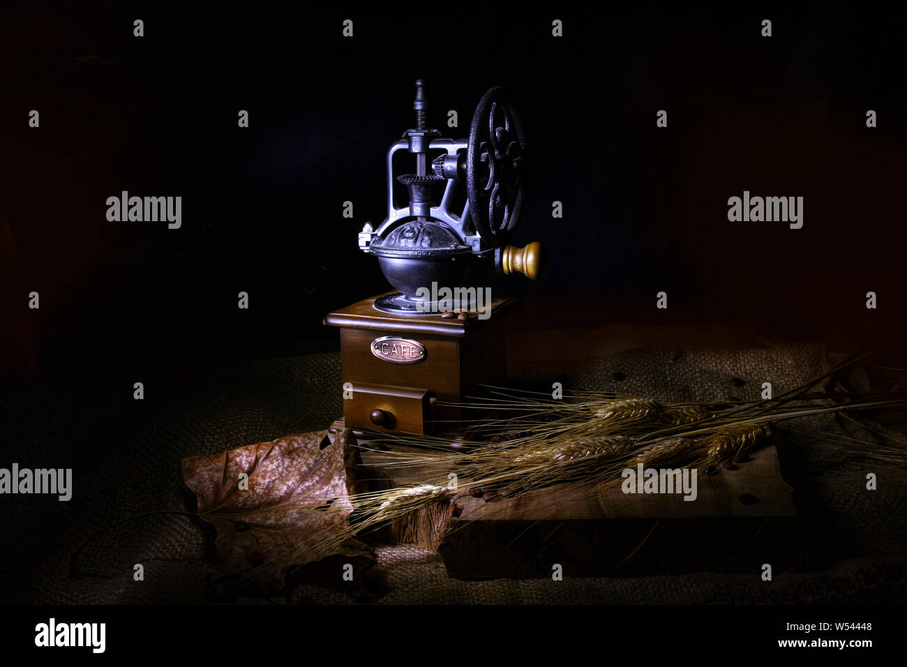 Stilizzata vintage macinino da caffè, foglie secche e spighe di grano su una tela ricoperta di tavolo in legno. Foto Stock