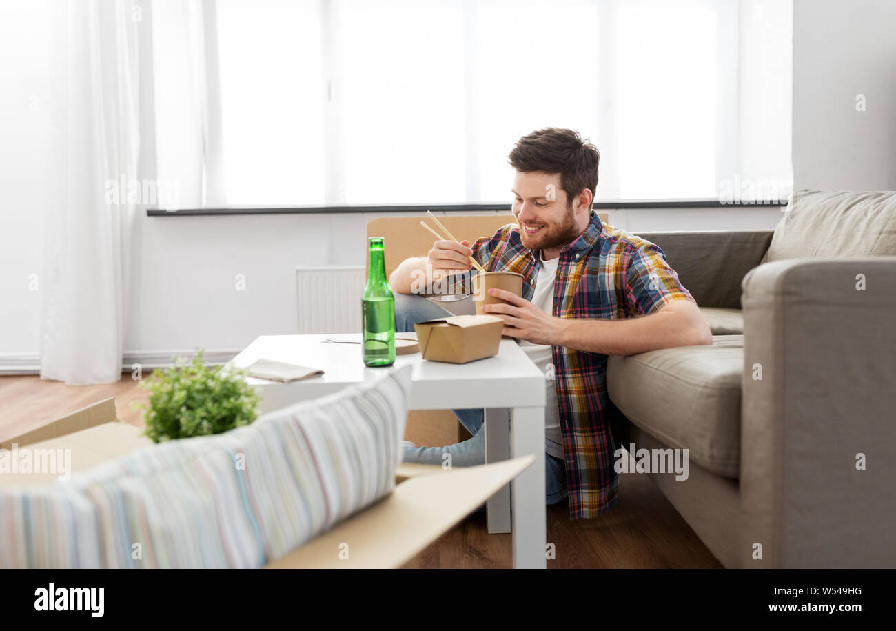 Uomo sorridente mangiare cibo da asporto a nuova casa Foto Stock