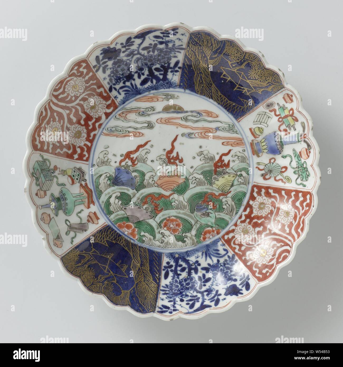 Piattino-piatto con lati scanalati e fiori e frutti di mare al di sopra delle onde, pirofila con parete nervata e bordo lobata, dipinta in underglaze blu e sullo smalto blu, rosso, verde, giallo, melanzana, nero e oro. Sul ripiano di un medaglione con prunus fiori e frutti di mare sopra le onde di vorticazione, la parete suddivisa in otto scomparti con la stessa decorazione sul lato opposto: lotus vite salvate contro una terra rossa, alberi fioriti con bird e butterfly, un paesaggio in oro contro un bleu poudré (polvere blu) Terra e fortunati simboli (treppiede, vaso con penne di pavone, pergamene, libri Foto Stock