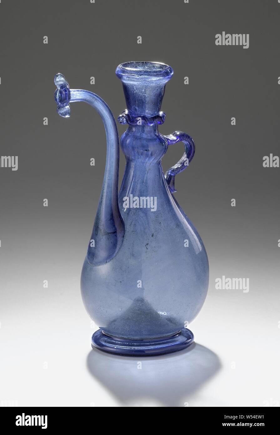 Beccuccio caraffa con pera-corpo sagomato, profondamente inserita inferiore. Cava ampia anello di supporto. Schiacciato lateralmente a forma di pera corpo, fondendo in un leggermente orlate nodus e basso leggermente svasata con il collo verso l'interno di un bordo risvoltato. Un nervato anello antigoccia è stata collocata intorno al collo. La alta, beccuccio ricurvo viene rifilato in apertura con una doppia ala. Piccolo, a forma di C orecchio., Anonimo persiano, c. 1700 - c. 1900, vetro, glassblowing, h 21.6 cm × d 13,5 cm Foto Stock
