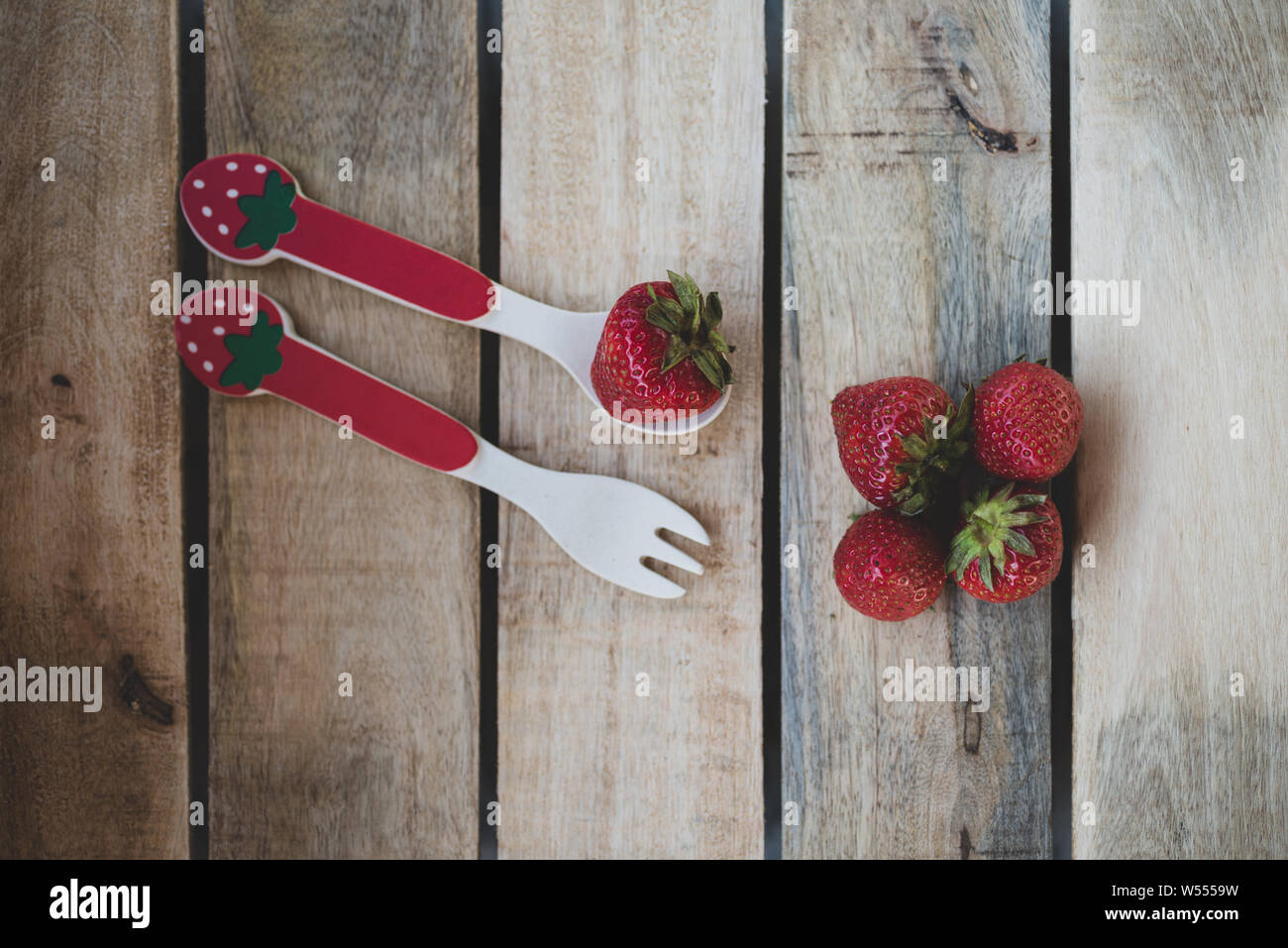 Cucchiaio e forchetta con una fragola su una tavola di legno Foto Stock
