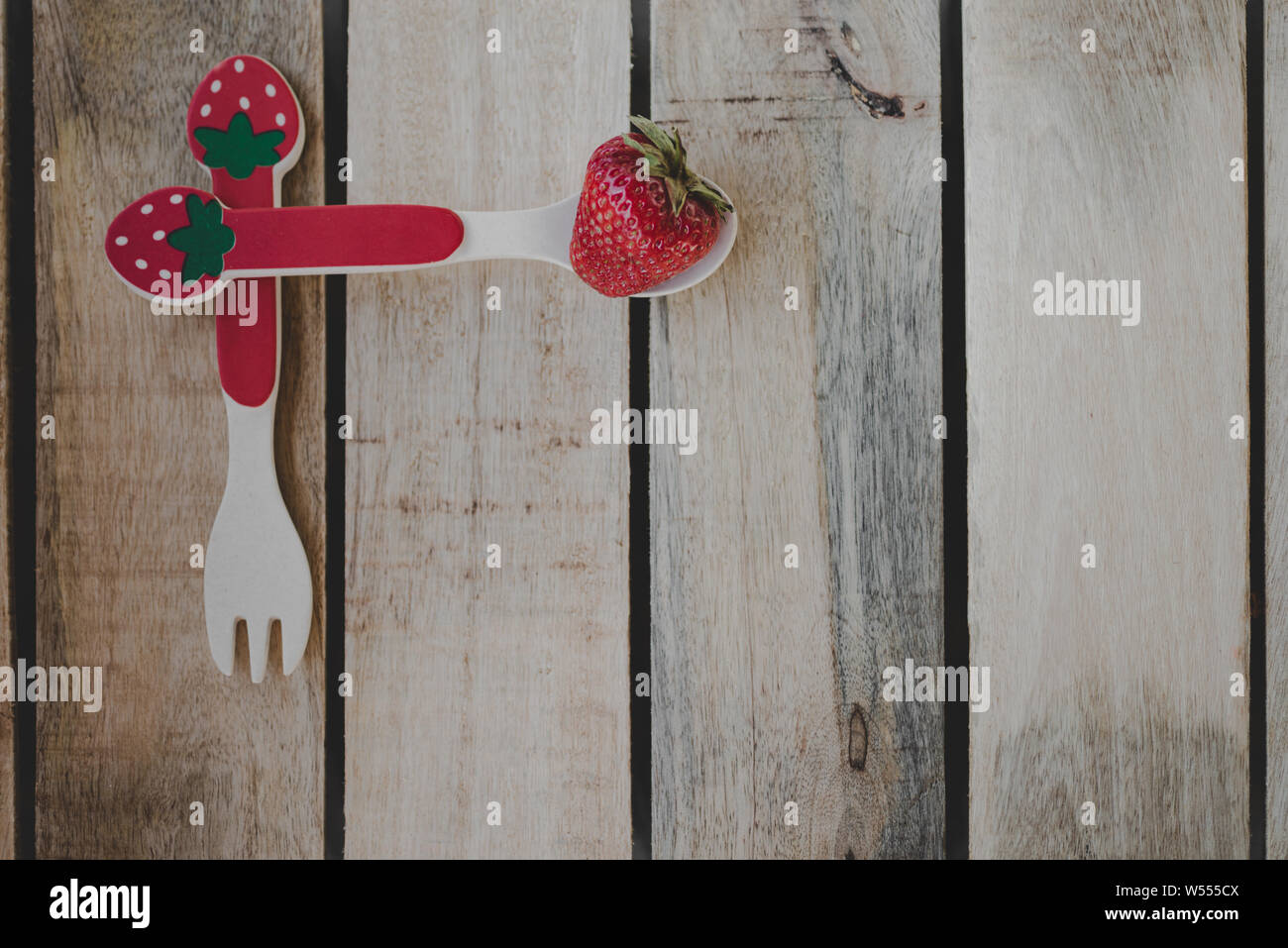 Cucchiaio e forchetta con una fragola su una tavola di legno Foto Stock