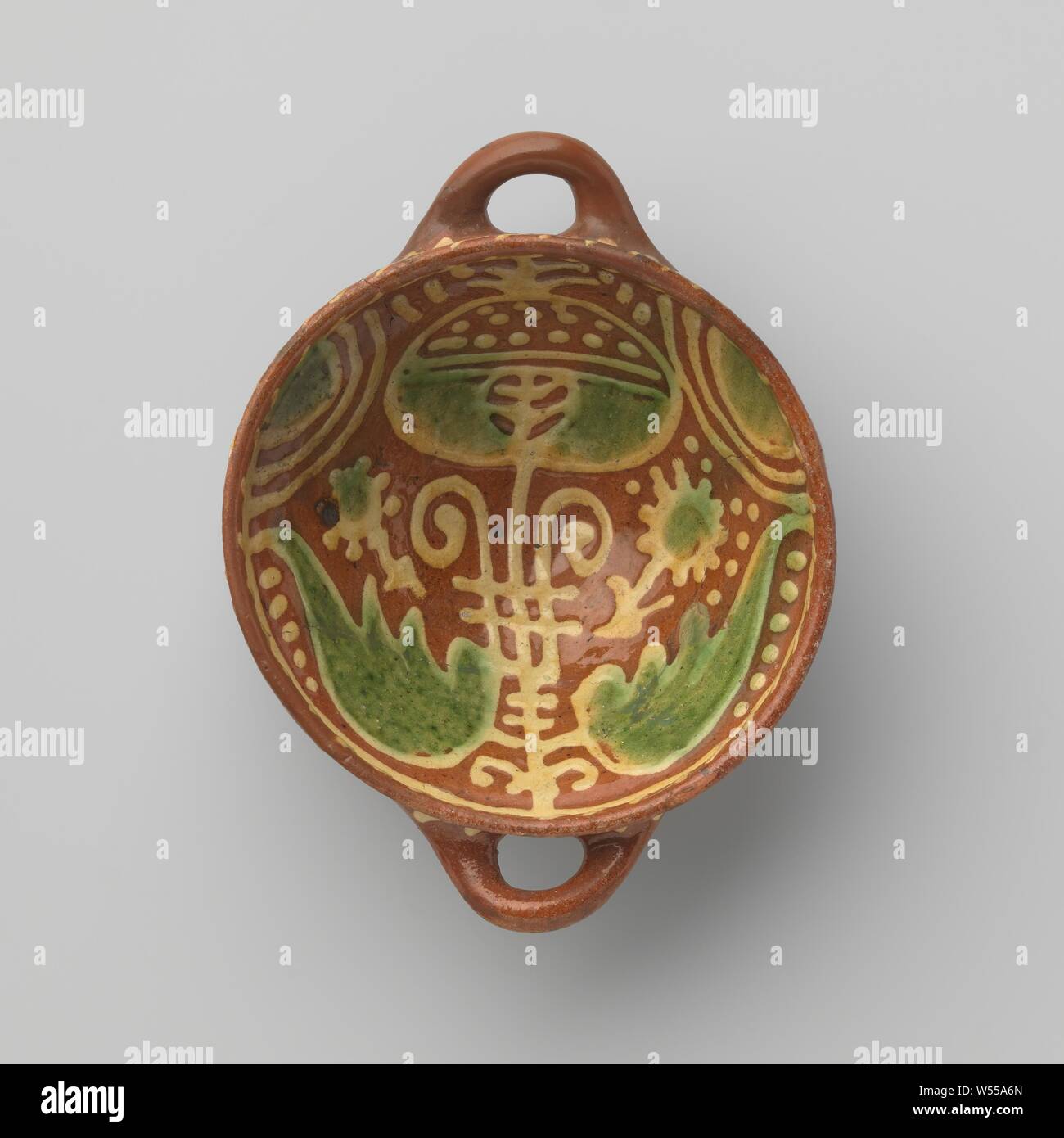 Papkom, piombo-terracotta invetriata papkom, con due orecchie. Il vaso è decorato con tecnica di fanghi nei colori giallo e verde con un fiore (semi di papavero?) con posti simmetricamente foglie. La tazza ha strisce lungo il bordo., anonimo, Olanda, c. 1600 - c. 1699, terraglia, piombo smalto h 7.5 cm × W 20,1 cm × d 15,5 cm Foto Stock