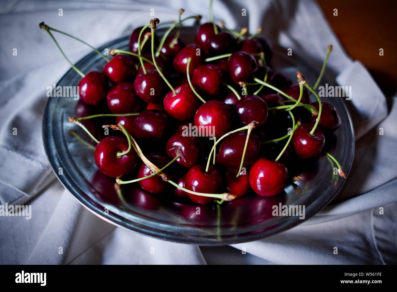 La ciliegia, rosso ciliegie mature nella piastra e sul tessuto, chiave di basso o fotografia scuro Foto Stock