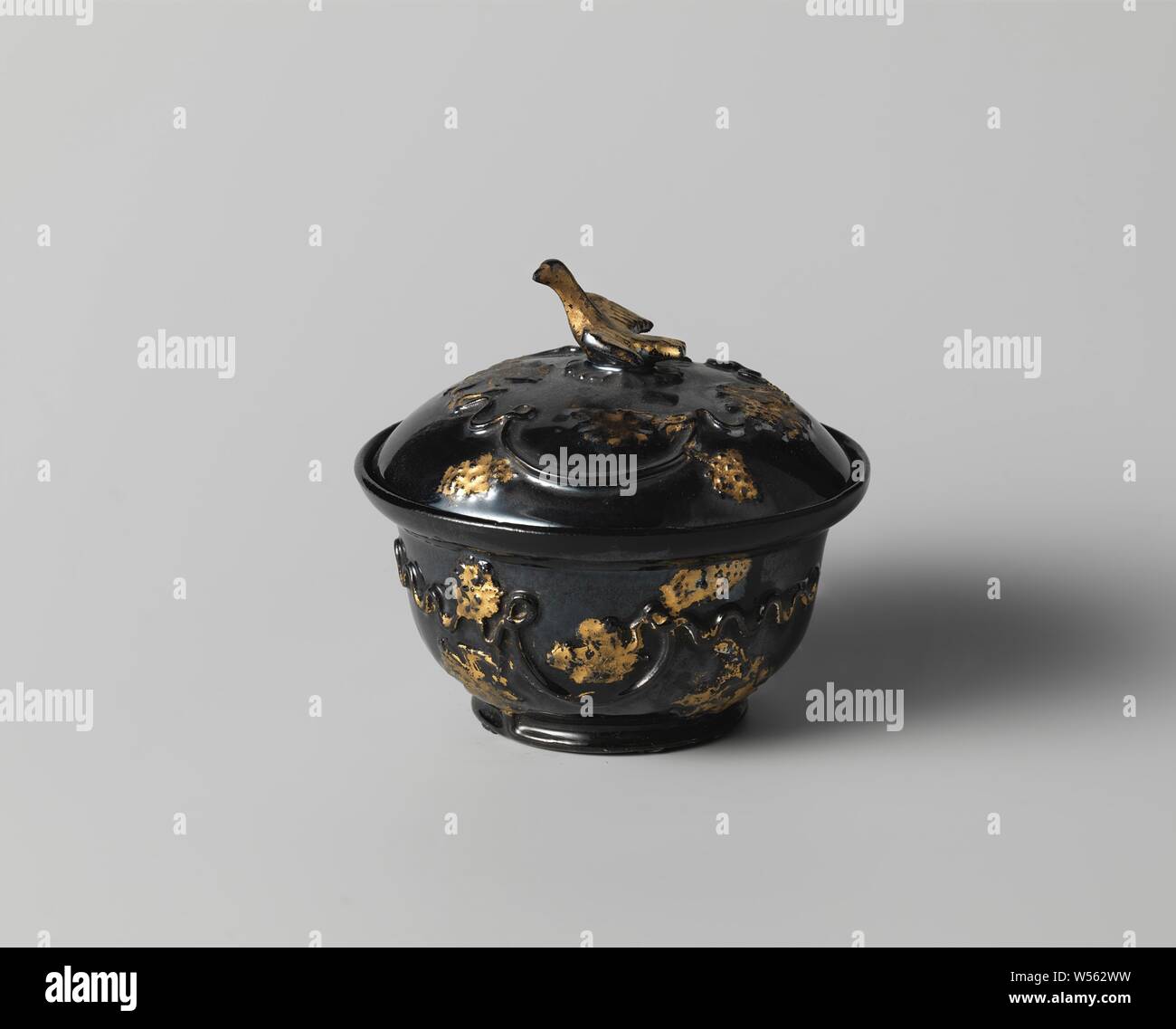 In terracotta con coperchio nero smalto opaco, un coperchio ricurvo. Il pomolo del coperchio ha la forma di un uccello con ali spiegate. Il coperchio è decorato a rilievo con una vite e il lavoro di foglia che è dorato sullo smalto in pochi luoghi., anonimo, Staffordshire, c. 1740 - c. 1770, terraglia, h 4.6 cm × d 9,4 cm Foto Stock