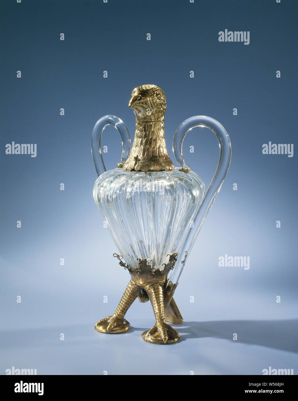 Decanter a forma di L'Aquila, vaso-corpo sagomato con grosse nervature, montato nella forma di un'aquila, con due gambe, una coda e una testa d'aquila d'argento dorato. Luci di coda, il collo e la testa sono incisi con scale, la coda, il collo e la testa con piume., anonimo, Germania (eventualmente), c. 1800 - prima del 1875, vetro, montuur, incisione h 23.5 cm w 18 cm d 12 cm Foto Stock