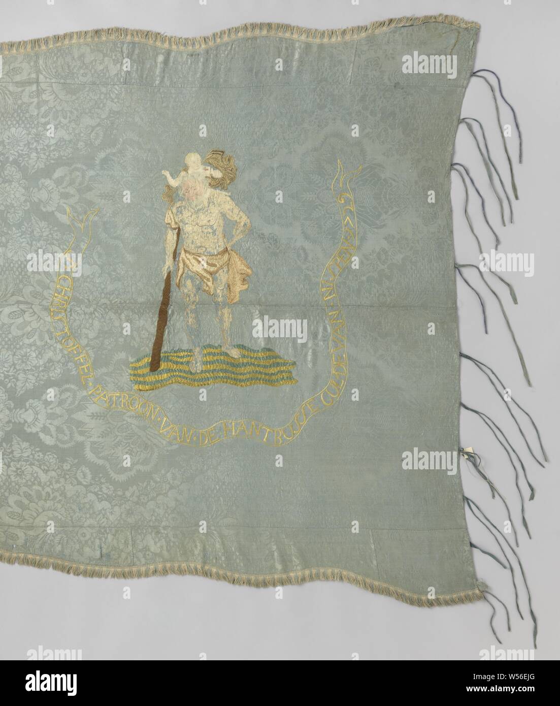 Banner di damasco blu con ricami di San Christoffel, un banner con didascalia ricamato sotto il ricamo di San Christoffel con Cristo Bambino: S. CHRISTOFFEL. PATTERN. Dal 'HANTBUS [0013] Gulde VAN NISPEN 1729', San Cristoforo con il bambino Cristo sulle sue spalle, guadare attraverso l acqua e portando il suo personale (palma), talvolta un eremita sorge sulla banca inoltre accanto a una cappella, una lanterna in mano, anonimo, Brabant (eventualmente), 1725 - 1729, seta e ricami, h 225 cm × W 143 cm h 50 cm × W 54 cm Foto Stock